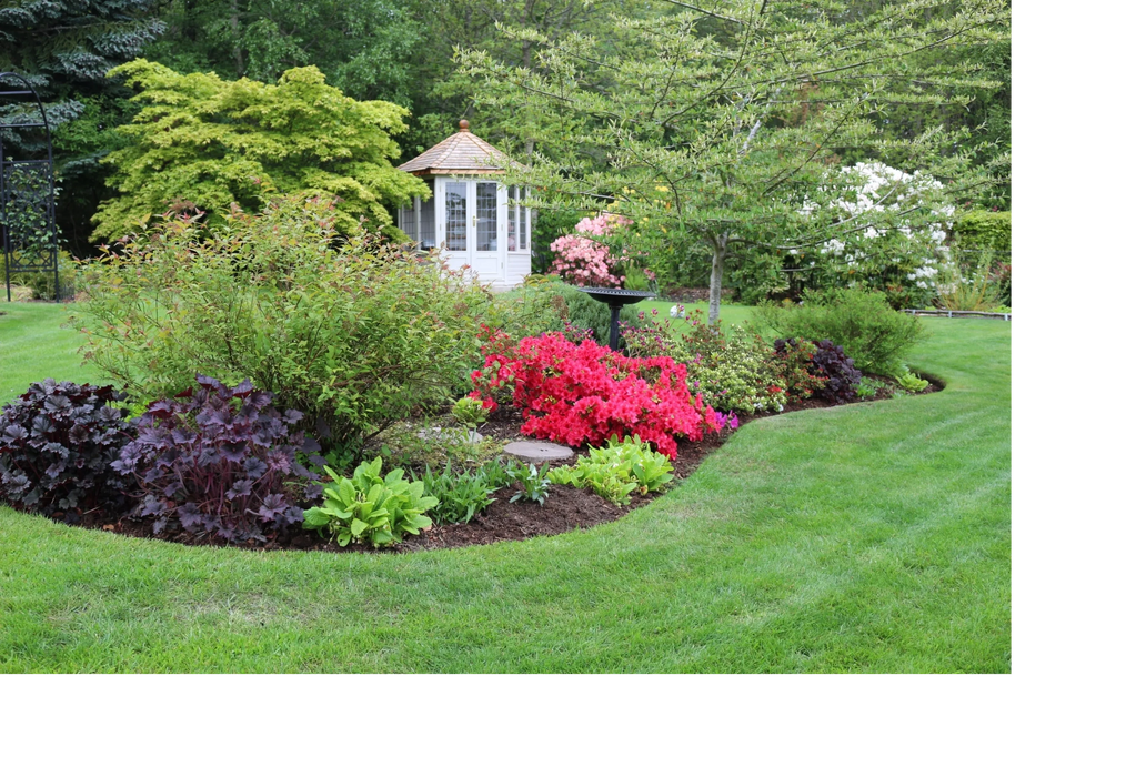 Photograph of a plant-filled flowerbed with a summerhouse in the background.