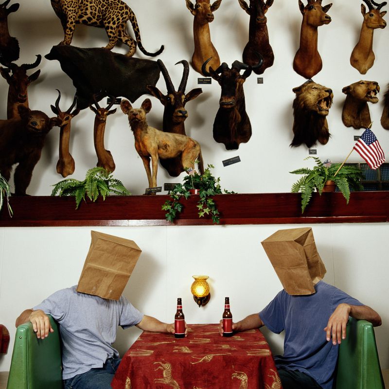 Picture of Crop bandmembers sitting in a diner with paper bags on their heads. On the wall above them are several taxidermied animals.