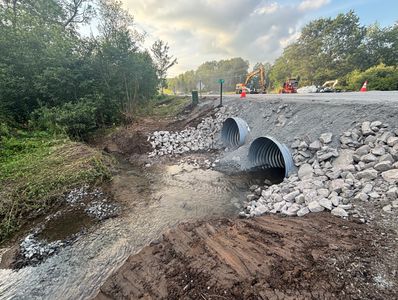 Newly installed culverts channel water under a rural road amid ongoing construction.