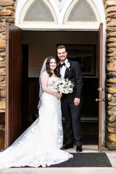 Newlywed couple smiling at the entrance of a stone building.