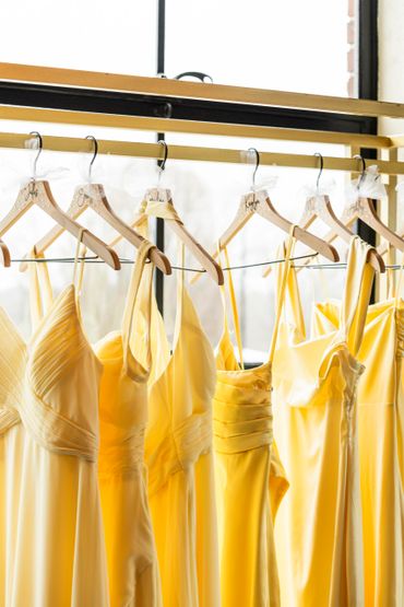 Yellow dresses hanging on wooden hangers by a window.