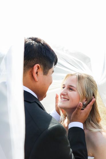Groom tenderly holds bride's face under the veil, sharing a loving moment.