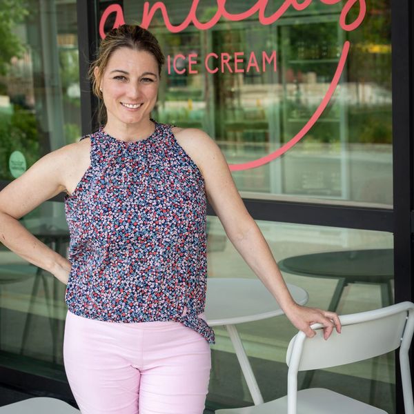 A woman in floral top and pink pants poses outside an ice cream shop smiling.