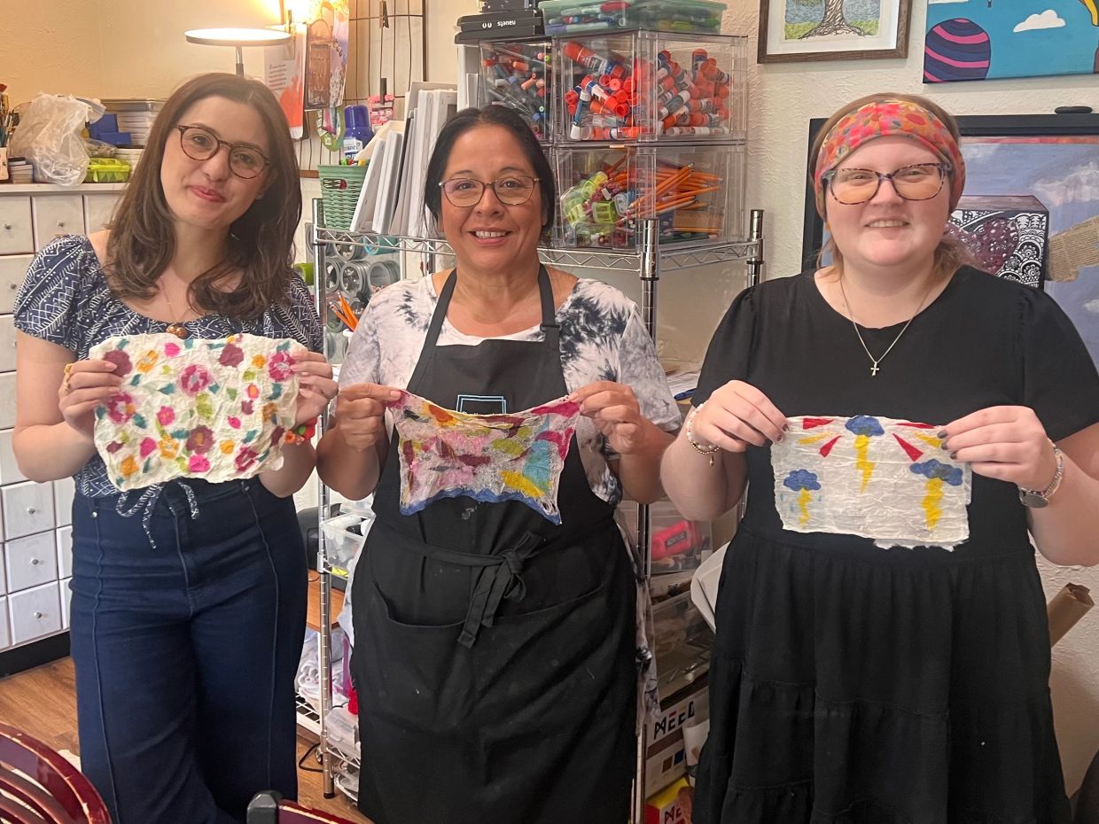 Three women holding colorful handmade paper sheets.