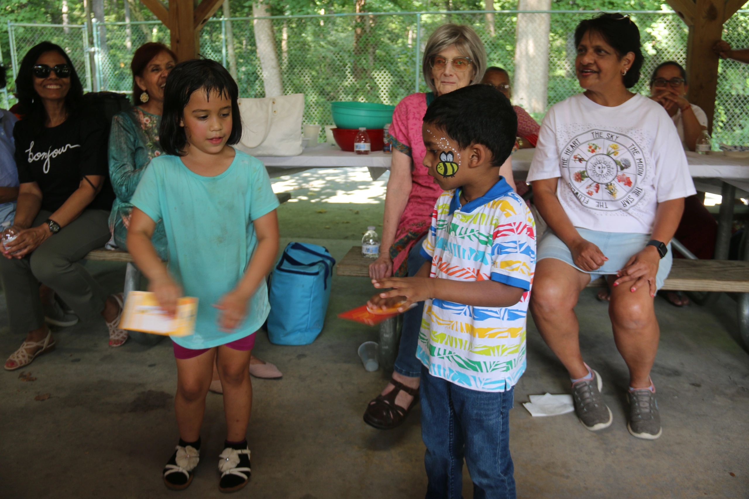Children with face painting and adults sitting in a pavilion.