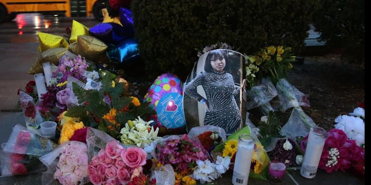 A memorial with flowers, candles, balloons, and a photo of a young woman.