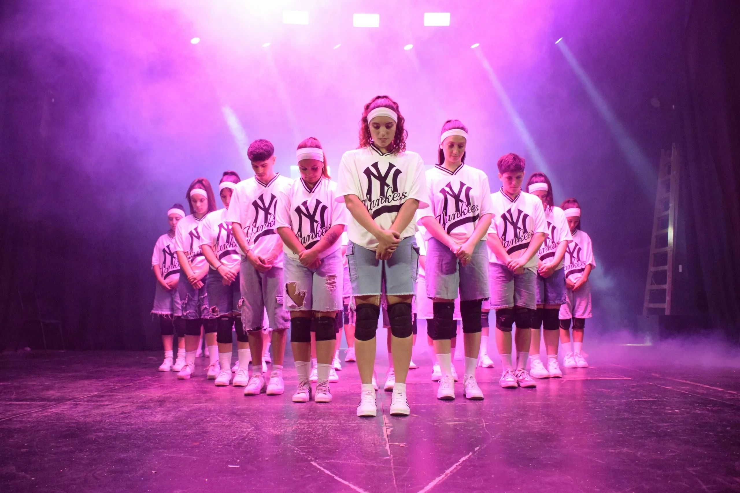 Dance group in coordinated outfits under purple stage lights.