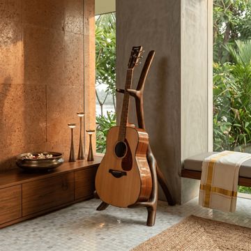 Acoustic guitar on a wooden stand in a cozy, sunlit room with natural decor.