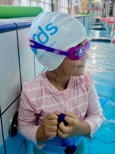 Child swimmer in pool with goggles and swim cap.