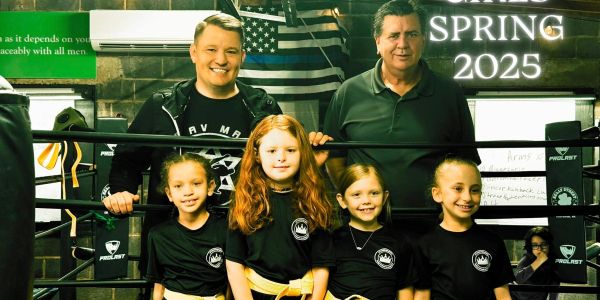 Group photo of five children and two men in a gym.