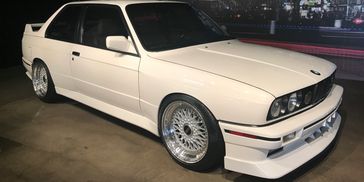 White BMW E30 car parked indoors with polished alloy wheels.