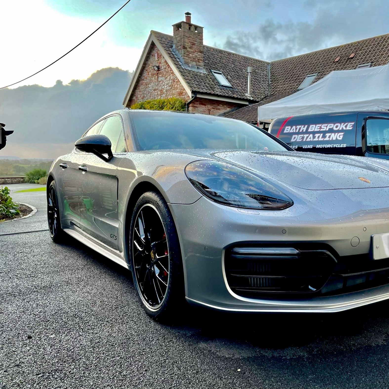 A sleek silver Porsche GT5 with black rims parked in front of a detailing van.