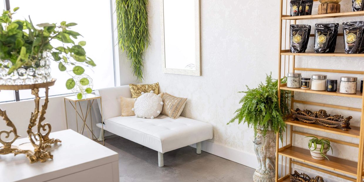 Bright, elegant room with white couch, gold accents, and lush green plants.