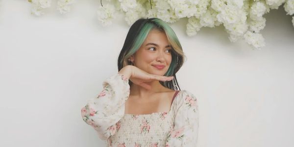 Young woman with green-tinted hair posing against a white floral backdrop.