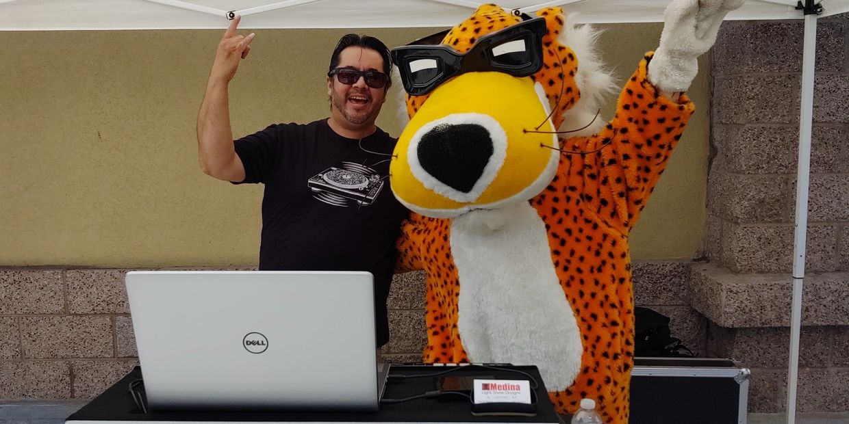 Picture of Owner/DJ & Chester Cheetah posing from behind the DJ booth.
