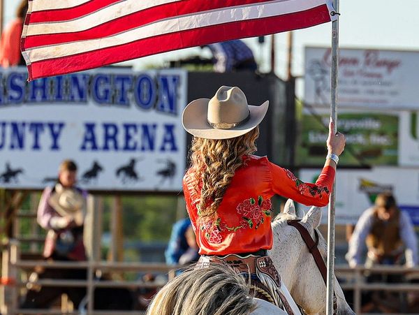 Woman on horseback holding an American flag at a rodeo arena.