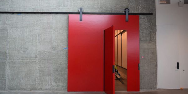 A partially open red sliding Chemical Proof door by Sing Core.