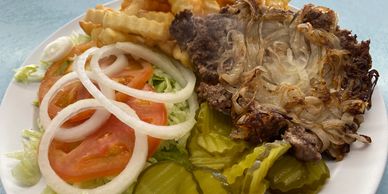 Smash burger with onions and pickles accompanied by crinkle cut french fries.