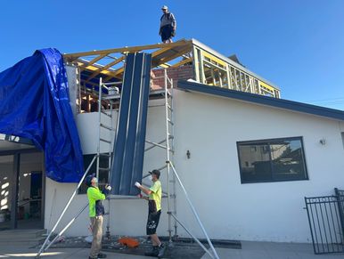 Workers installing roofing panels on a house under construction.