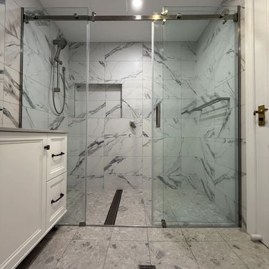 Modern bathroom with marble tiles and glass shower doors.