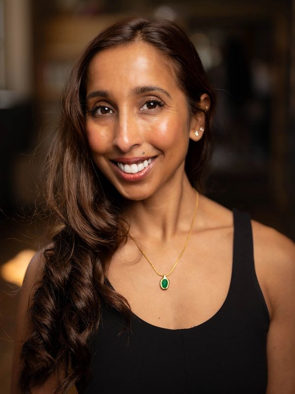Smiling woman with long hair and green pendant necklace.