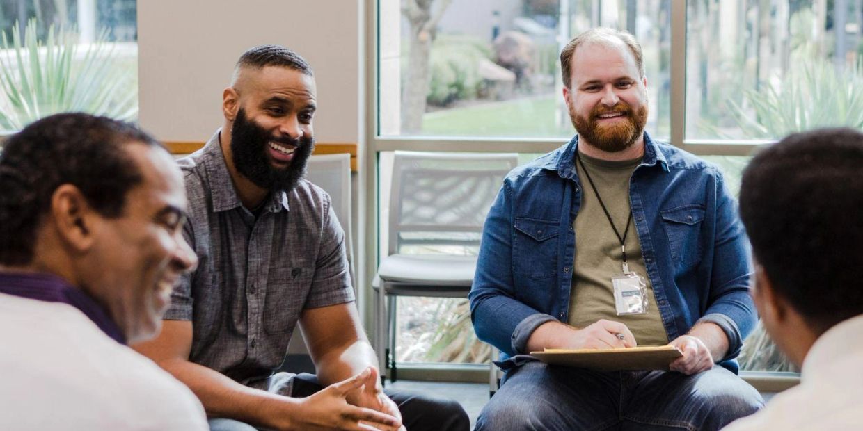 Four men sitting and smiling in a casual meeting.