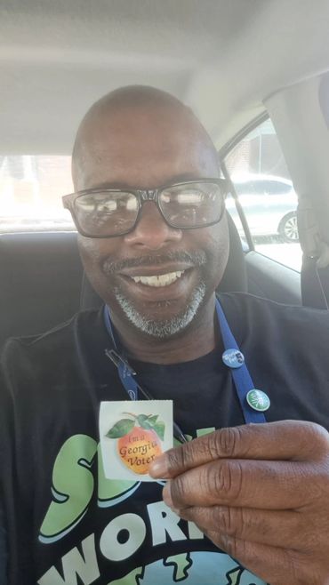 Man smiling in a car holding a Georgia Voter sticker.