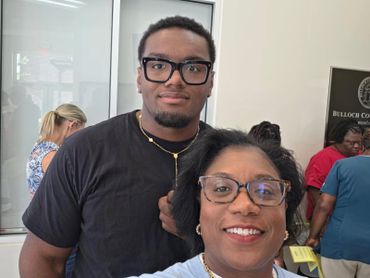 A smiling woman and a young man posing indoors at an event.