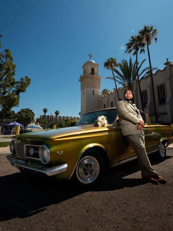 Man in suit leaning on classic car with church in background.