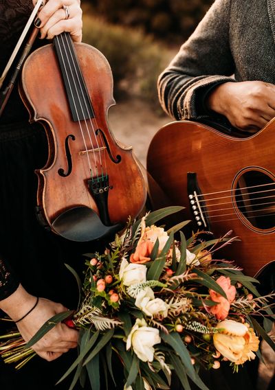 Two musicians holding guitar and violin with a bouquet of flowers.