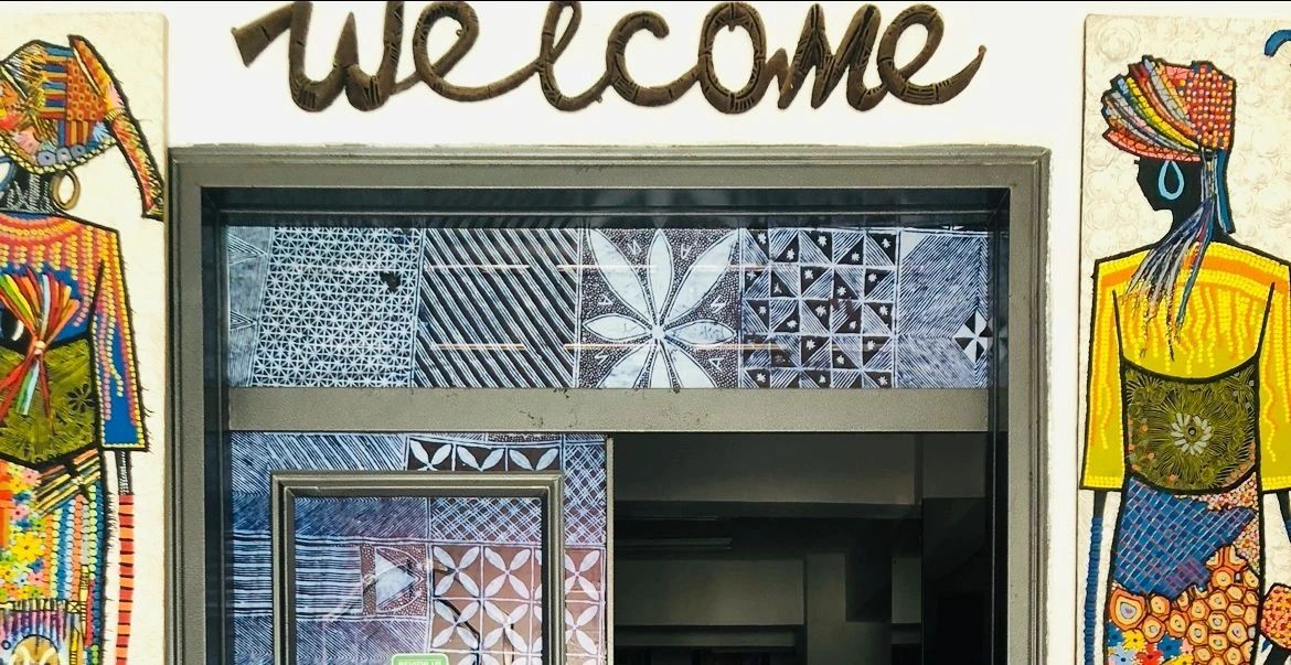 Image of the word "welcome" above an entrance and a person standing on each side of the door.