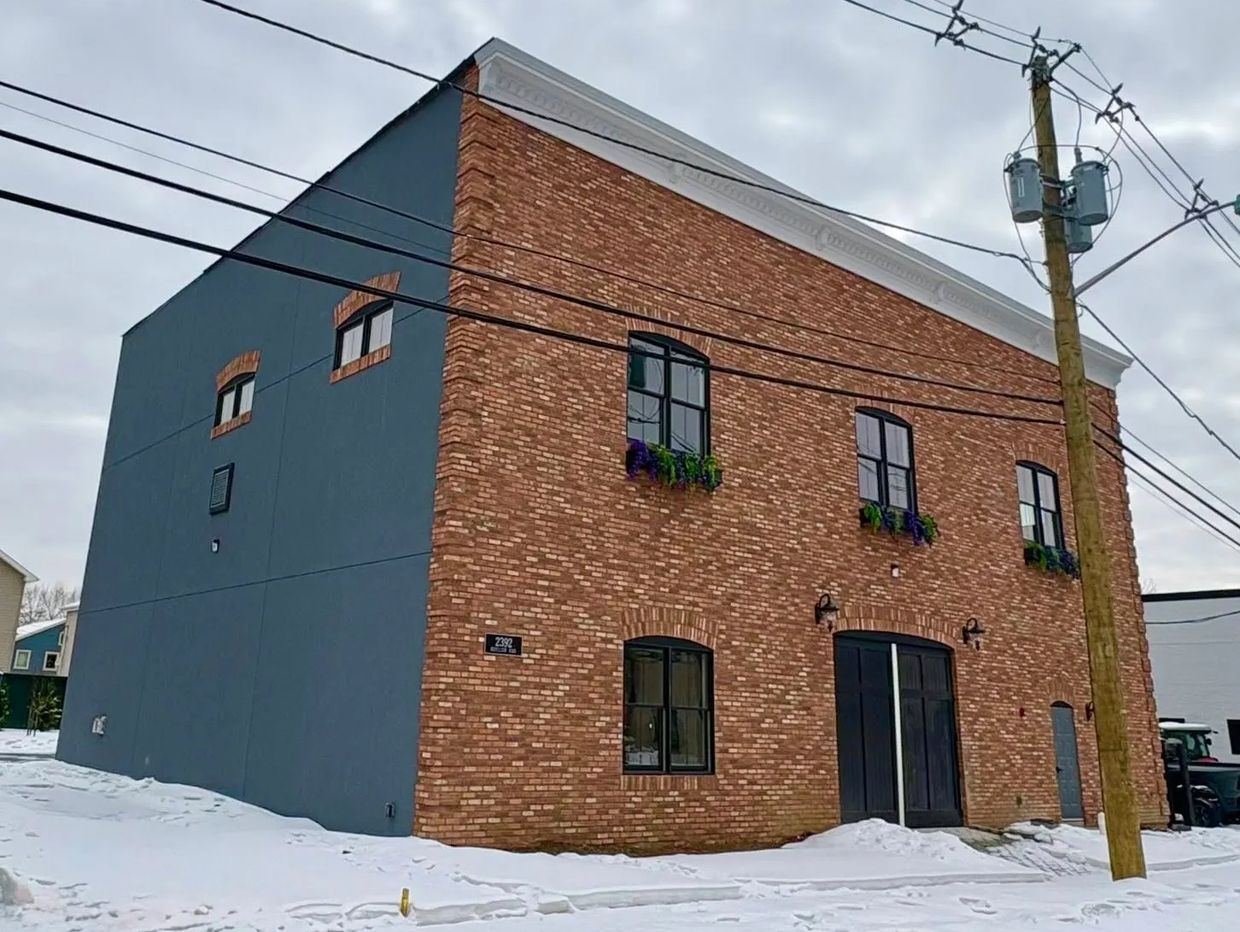 Brick building with black windows and flower boxes in a snowy setting.