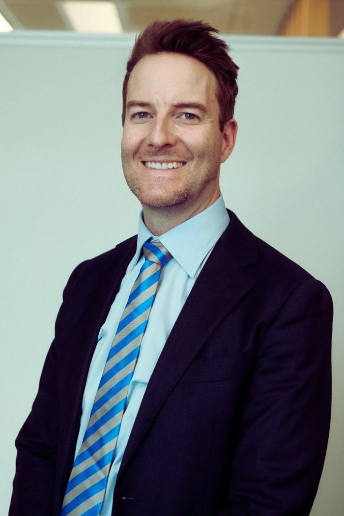 Smiling man in a suit with a striped blue tie.