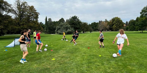 Kids practicing soccer drills on a grassy field under a cloudy sky.