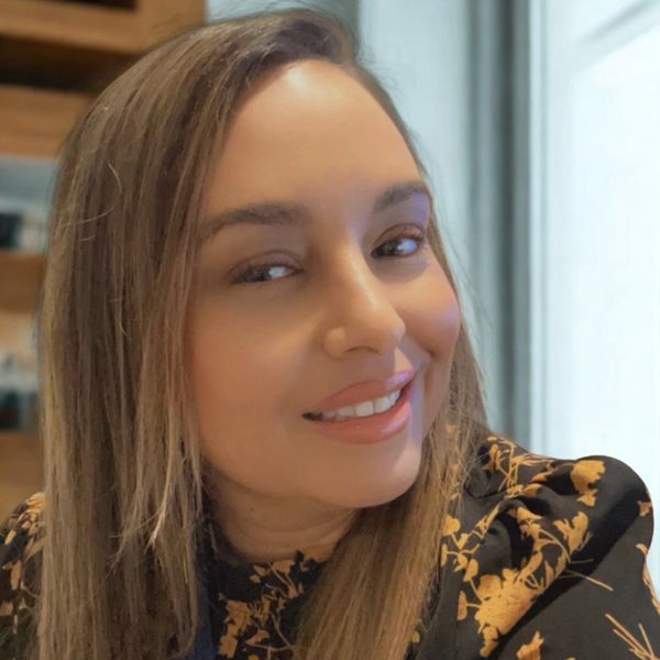 A woman smiling warmly with long hair and a floral-patterned top.