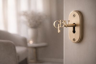 Elegant golden key labeled GBV in a door lock with a blurred cozy interior background.