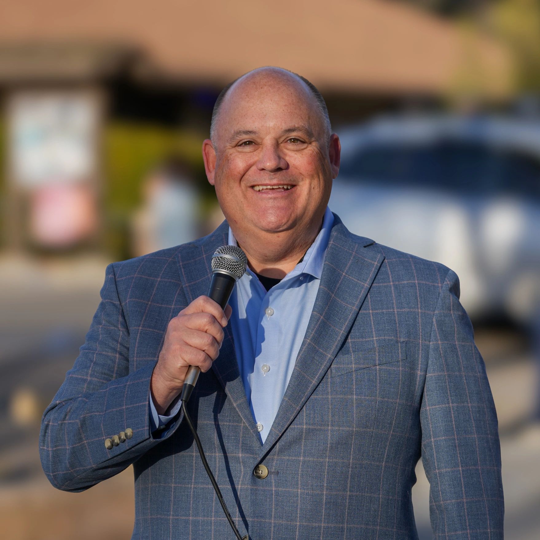Smiling man in a blue checkered jacket speaking into a microphone.