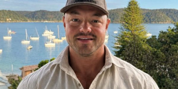 Man in white shirt and cap near marina with boats.