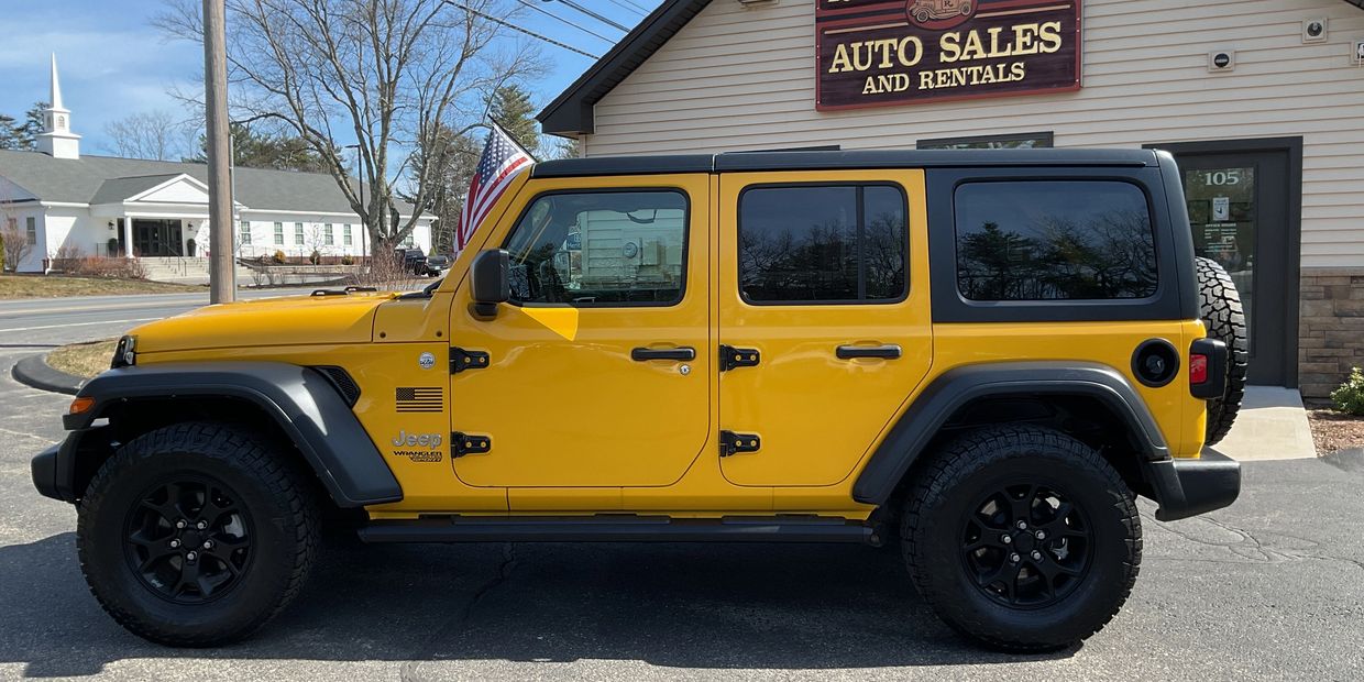Yellow Jeep Wrangler parked outside an auto sales and rentals shop.