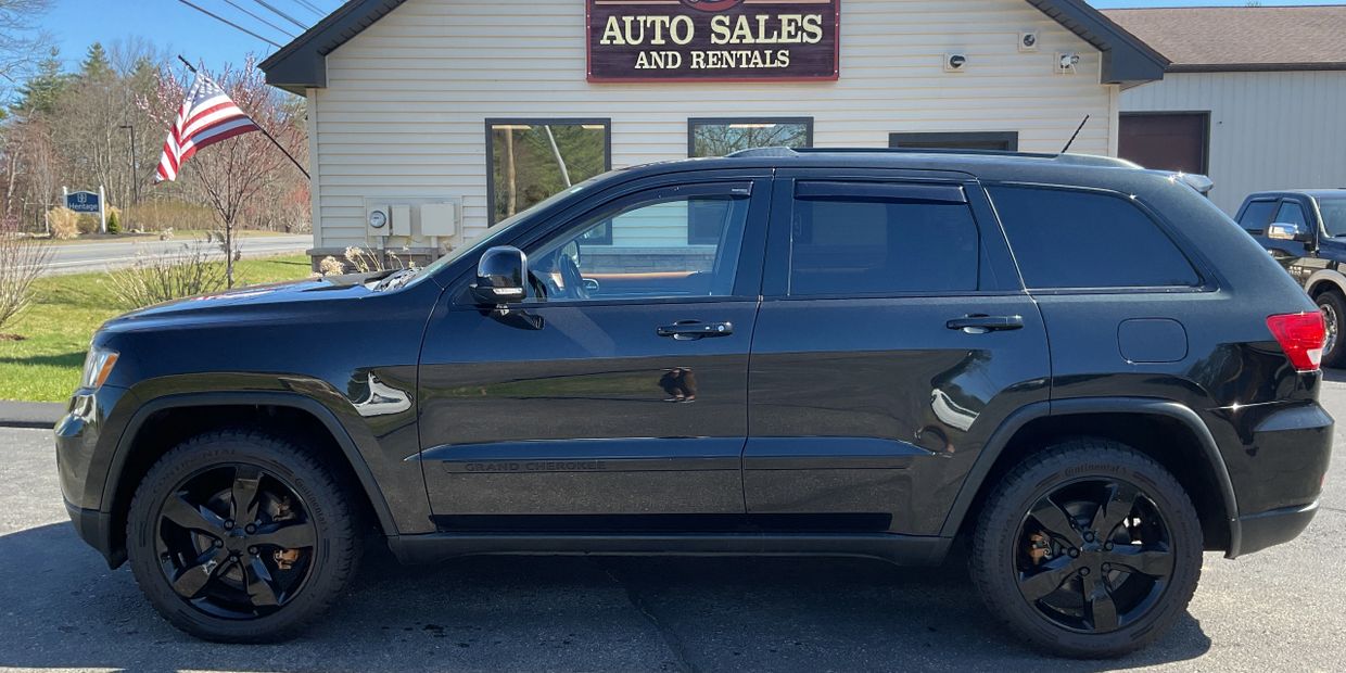 Black Jeep Grand Cherokee parked at an auto sales and rentals lot.