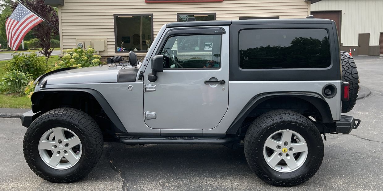 Gray Jeep Wrangler parked outside a building with an American flag nearby.