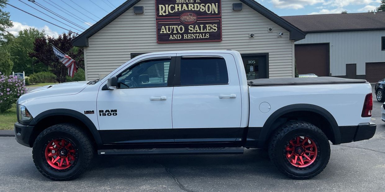 White RAM 1500 truck with red rims parked outside Richardson Auto Sales.
