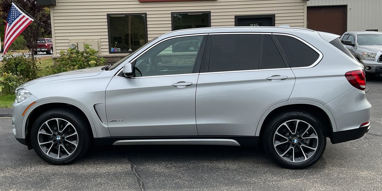 Silver BMW X5 parked in front of a building with an American flag.