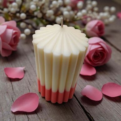A decorative two-tone candle surrounded by pink rose petals and flowers.