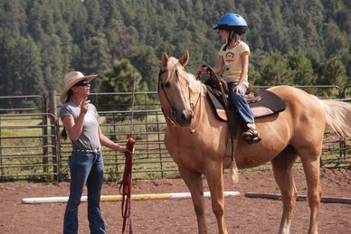 Girl on horse with instructor in outdoor arena.