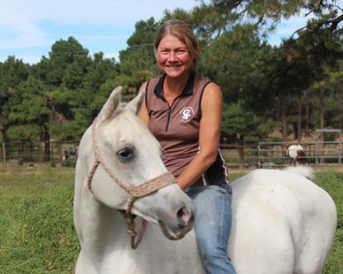 Woman smiling on a white horse outdoors.