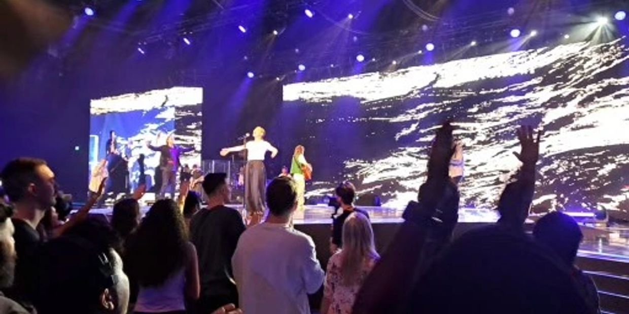 Crowd enjoying a live concert with performers on stage and colorful lights.