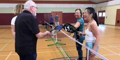 Freida Yueh and three others playing pickleball in a wood floor gym with temporary nets