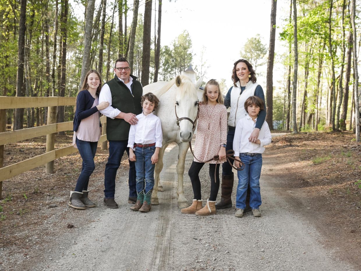 a family photo taken with a white horse in a driveway with a 3 board fence 