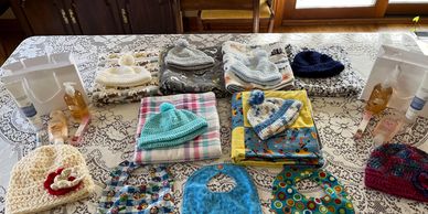 Handmade baby hats, blankets, bibs, and care items displayed on a table.
